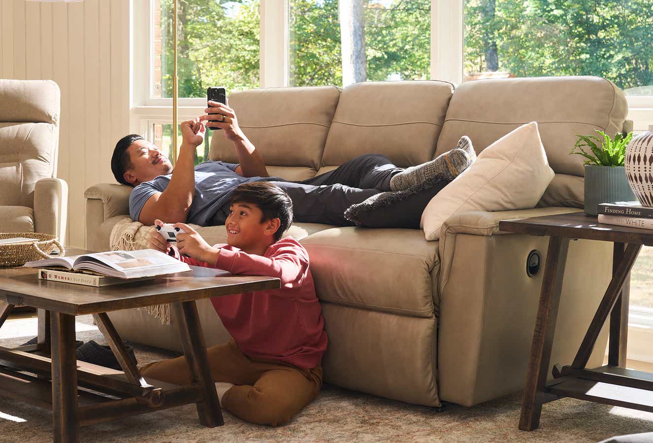 a man laying on a La-z-boy sofa on his phone